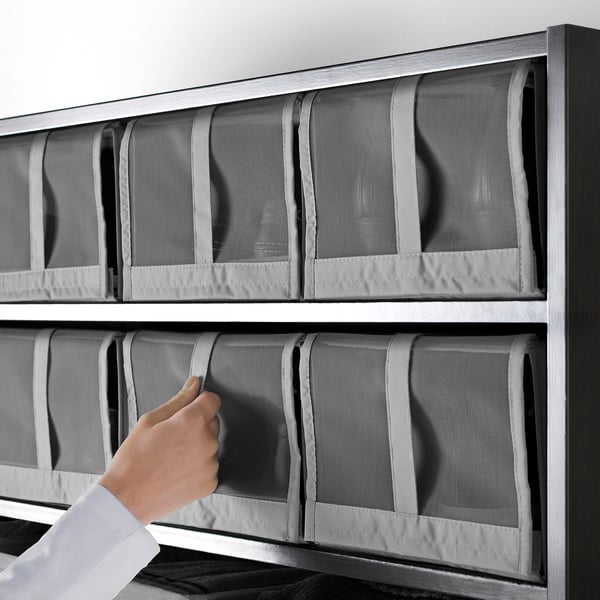 Person som placerar SKUBB-skokartonger i mesh på hyllan. Lådorna är organiserade och luft cirkulerar genom nätet.