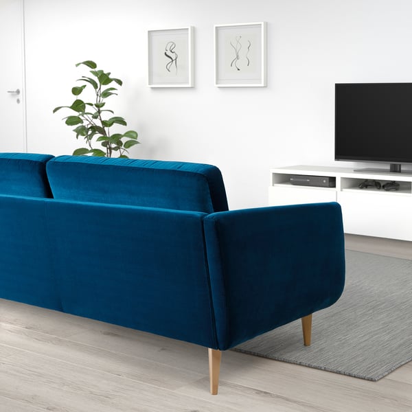 Ett modernt vardagsrum med en blågrön sammetssoffa, träben och en tv-bänk.