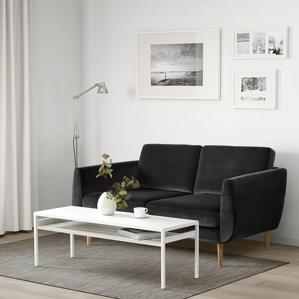 Modernt vardagsrum med mörkgrå sammetssoffa, vitt soffbord och svartvit väggkonst.