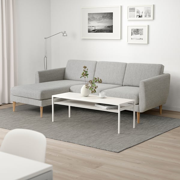 Ett modernt vardagsrum med en grå schäslong, soffbord och foton, som skapar en mysig, minimalistisk atmosfär.