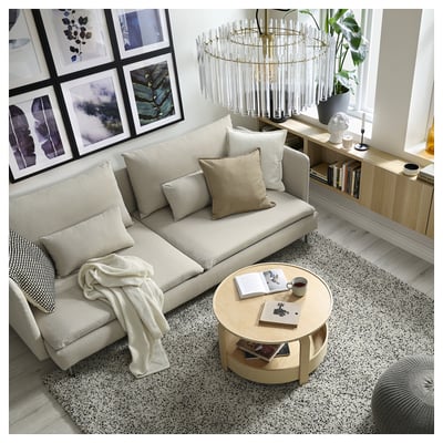 Modern vardagsrum, en beige SÖDERHAMN-soffa med kuddar, ett runt träbord med böcker och en kopp, inramad väggkonst och en stilren kristallkrona.