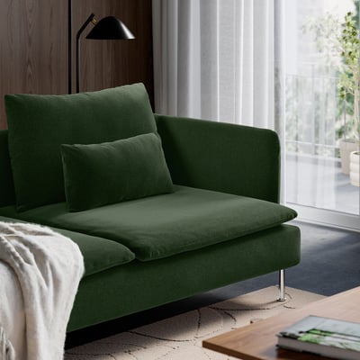 Grön soffa med kuddar nära ett fönster, som erbjuder en mysig sittgrupp med modern design.