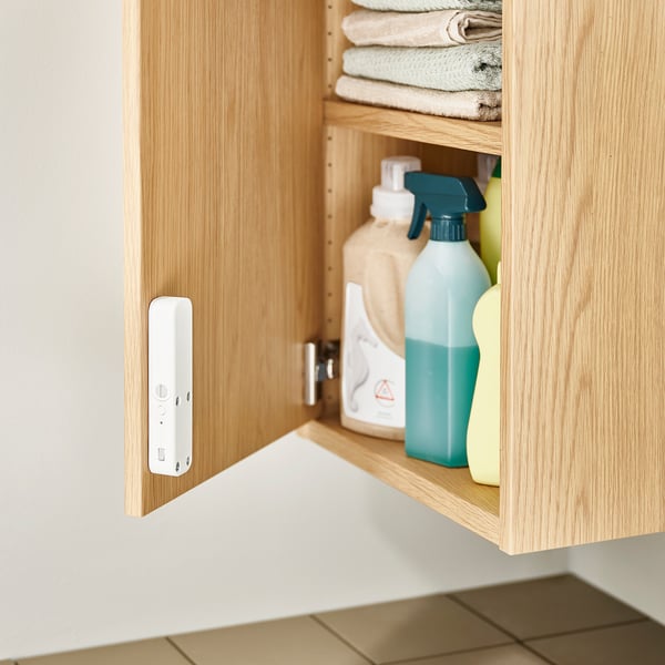 Ett öppet skåp i ljust trä som innehåller rengöringsmedel och vikta handdukar. Ett vitt SOLSTOL-lås är monterat på insidan av skåpdörren.