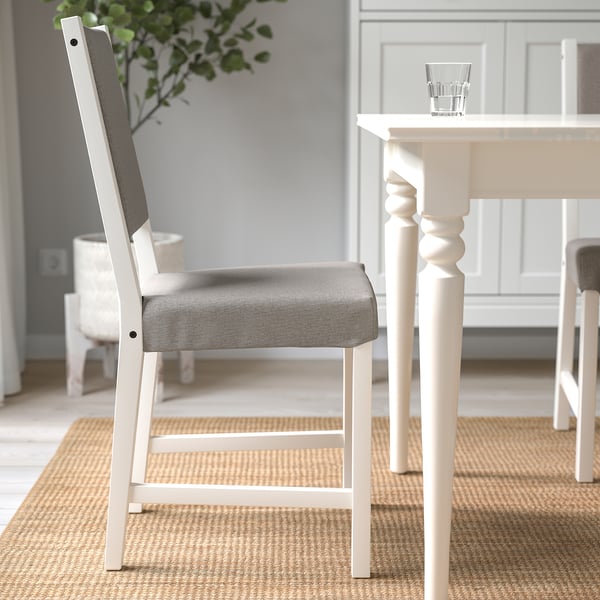 Modern matgrupp med vit stol med grå stoppad sits, placerad nära ett bord med ett klart glas och en växt.