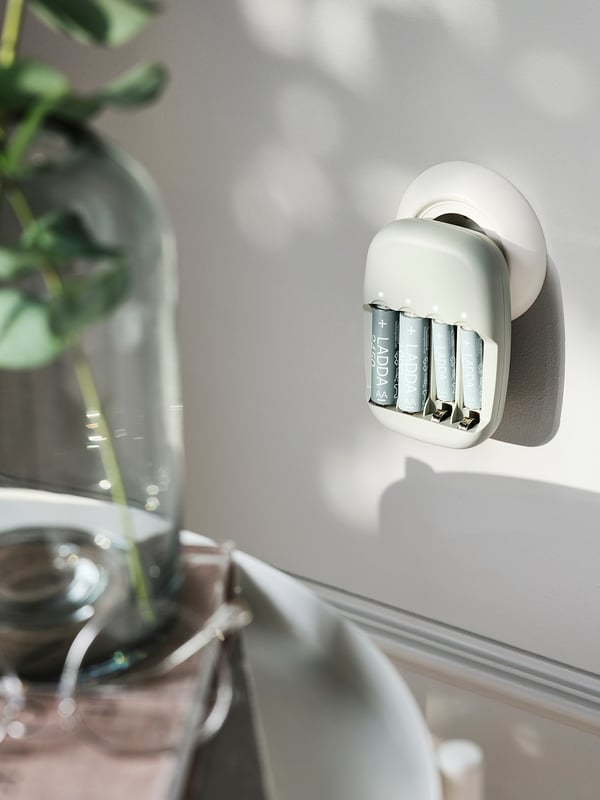 Vit STENKOL batteriladdare, tillverkad av återvunnen plast, fäst på en vägg, med 4 platser för laddning av batterier.