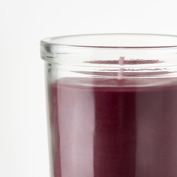 Doftljus med glasbehållare, mörkrosa nyans, reflekterande mjukt ljus, vilar på en vit yta.