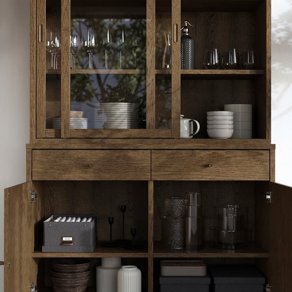 Träskåp med glasdörrar som visar tallrikar och glas. Har lådor och hyllor för förvaring, samt invändig belysning förberedd.