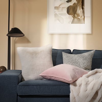 Ett modernt vardagsrum, en grå soffa prydd med TORPSPIREA-vit , mjuk kudde och en rosa kudde, som komplementerade en mysig, texturerad vit pläd.