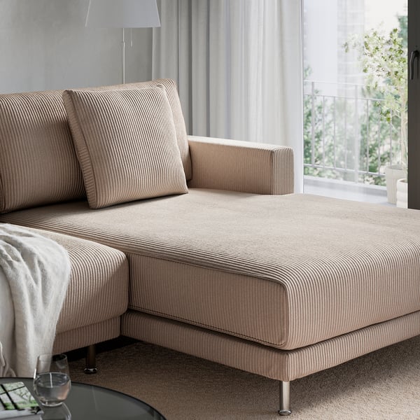 Beige UPPÅKRA sektionssoffa med kuddar nära fönstret, som erbjuder en mysig, inbjudande sittplats.