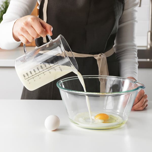 Personen häller mjölk från en mätkanna i en skål med ett ägg. Kannan har markeringar för att mäta vätska.