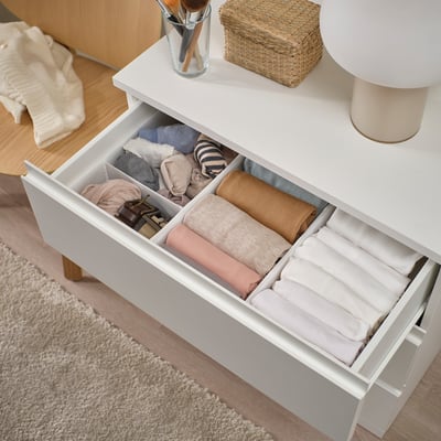 Organisateur de tiroir ouvert avec des vêtements pliés. Des séparateurs séparent les chaussettes, les pulls et les accessoires.