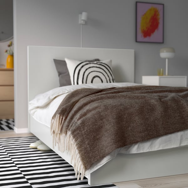 Cosy bedroom with colourful bed, striped rug, abstract art, bedside table, and lamp.