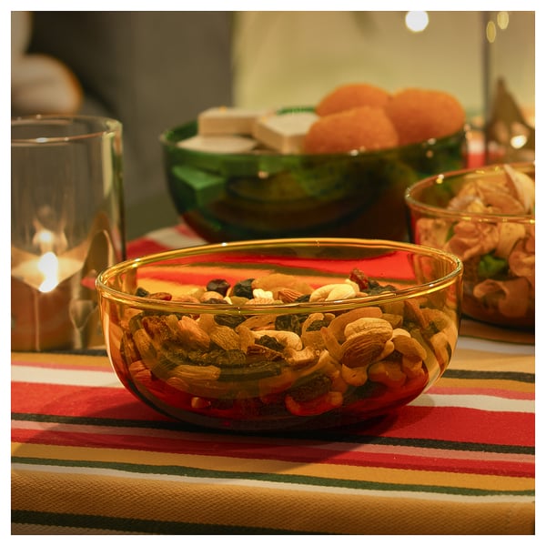 Colourful bowl with mixed nuts on a striped tablecloth, lit candle nearby.