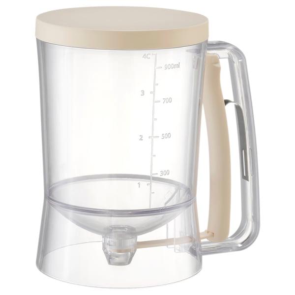 A BAKTIDER measuring jug, light beige, with clear markings, a silicone spout, and a stainless steel spring, designed for precision batter dispensing.