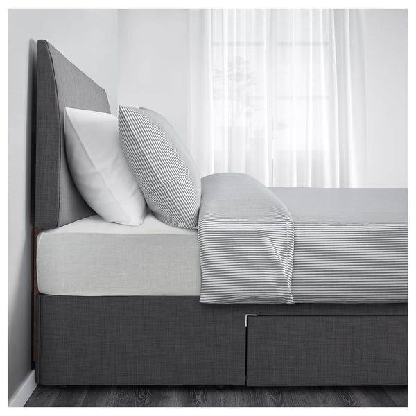 Modern bed with striped linens and grey headboard, featuring a pull-out storage drawer underneath.