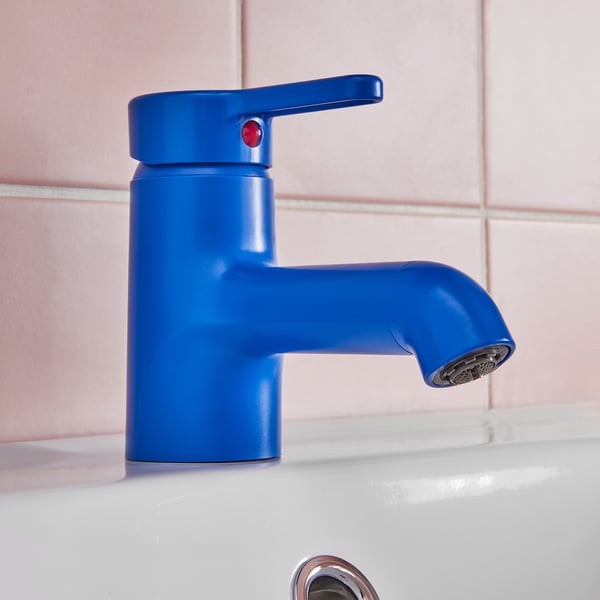 Bright blue modern tap with red switch on white sink against pink tiles.