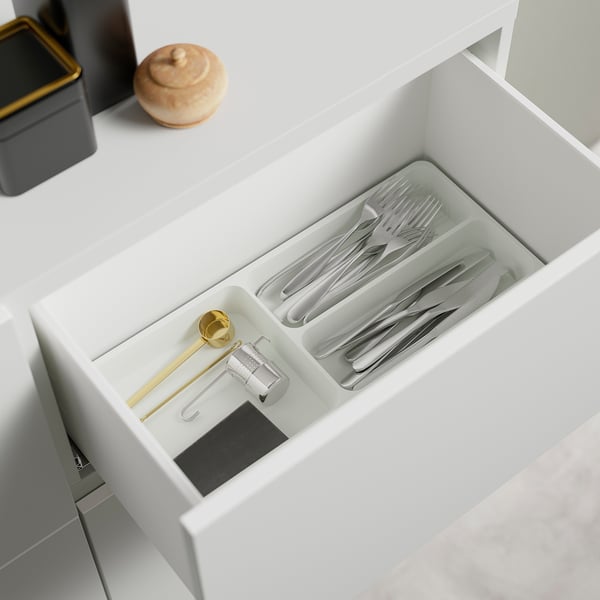 Open drawer with utensils: forks, knives, spoons, measuring spoon, can opener, in white BESTÅ organiser.