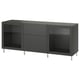 An ikea BESTÅ storage unit in dark gray with glass doors and metal legs. It adjustable shelves, two drawers, and a modern, sleek design.