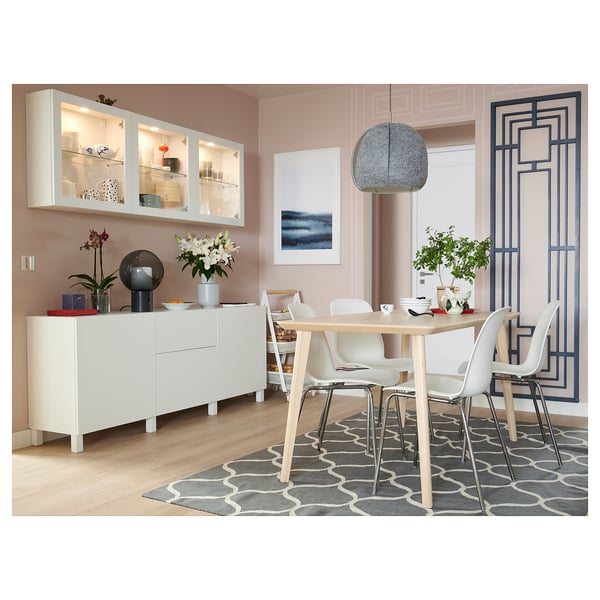 Modern dining room with white BESTÅ storage, light wood table, white chairs, geometric rug, pink walls, and hanging light fixture.