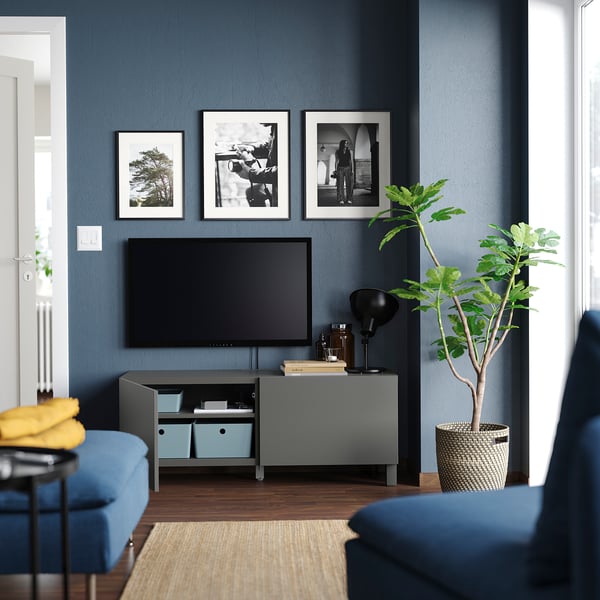 Modern living room with grey BESTÅ tv bench, blue sofa, and black & white photos on dark blue wall.