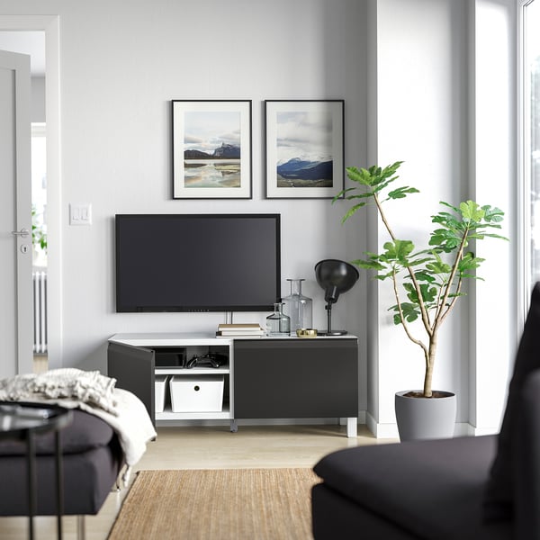 Modern living room with a black BESTÅ tv stand, flat-screen tv, two framed nature pictures, a tall green plant, and grey walls.