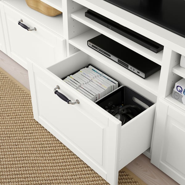 White BESTÅ tv unit with open drawer showing dvds and gaming controllers, black soundbar on top shelf.