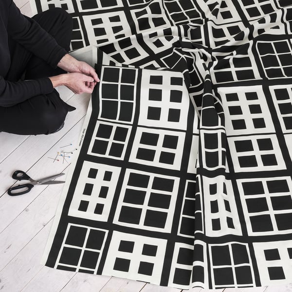Person crafting with geometric-patterned fabric, scissors, and pins on a wooden floor.