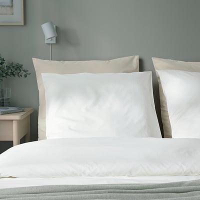 Calm bedroom with three DVALA white cotton pillows against turquoise wall. Small bedside table with glass vase and book beside bed.