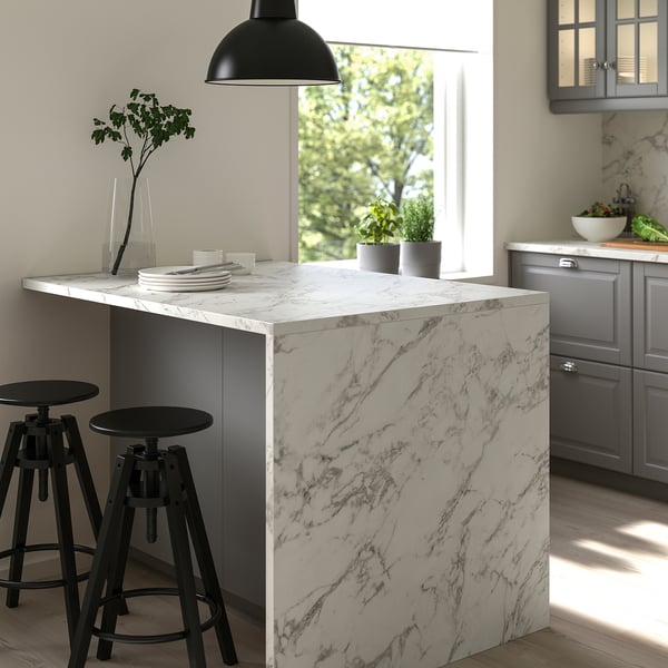 Modern kitchen with marble-patterned EKBACKEN island, black stools, hanging lamp, grey cabinets, and floral view through window.