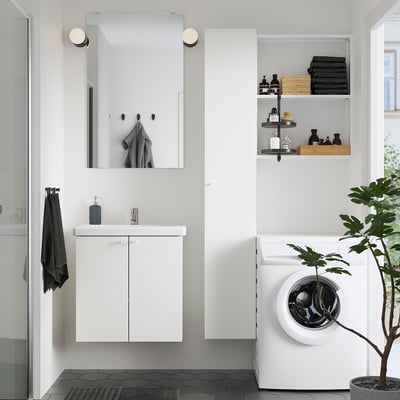 Modern bathroom with ENHET storage, mirror, towels, and stacked clothes. Large washer, plant, black floor tiles.