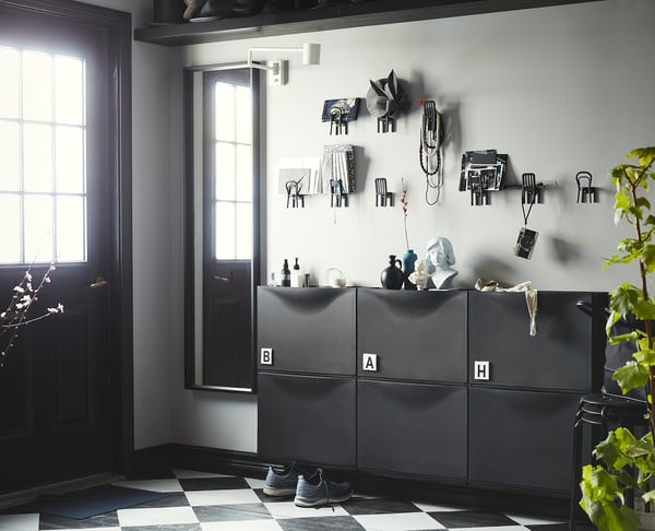 Modern entryway with black/white decor, grey storage, wall hooks, chequered floor, black door, plant.