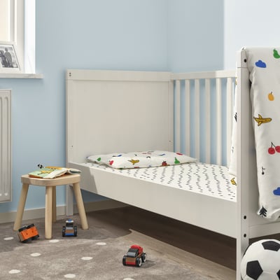 GRÖNFINK cot with tree sheet in blue room. Wooden stool & toy cars on rug.