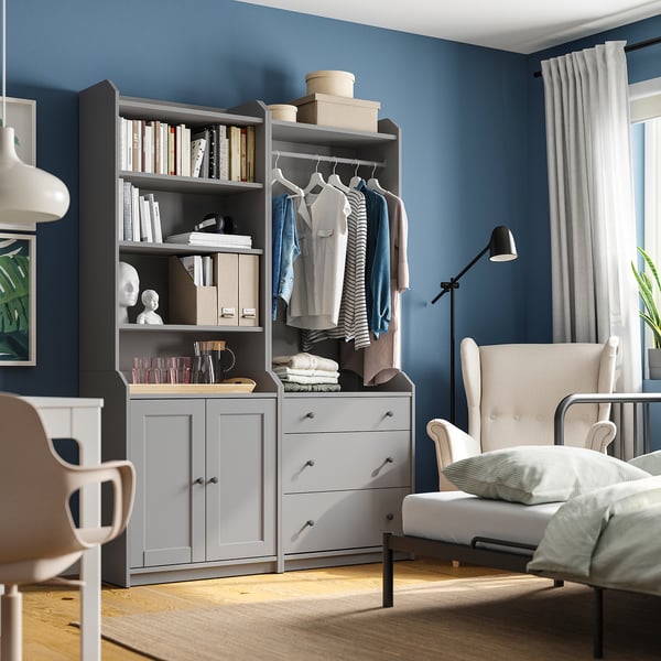 Modern bedroom with grey HAUGA storage, clothes, books, and decor. Blue walls, wooden floor.
