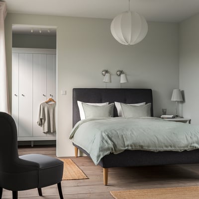 Minimalist bedroom with grey IDANÄS bed, pendant light, black chair, and wardrobe.