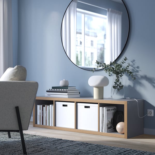 KALLAX shelf with books, lamp, plant. Mirror, chair. Modern living space.