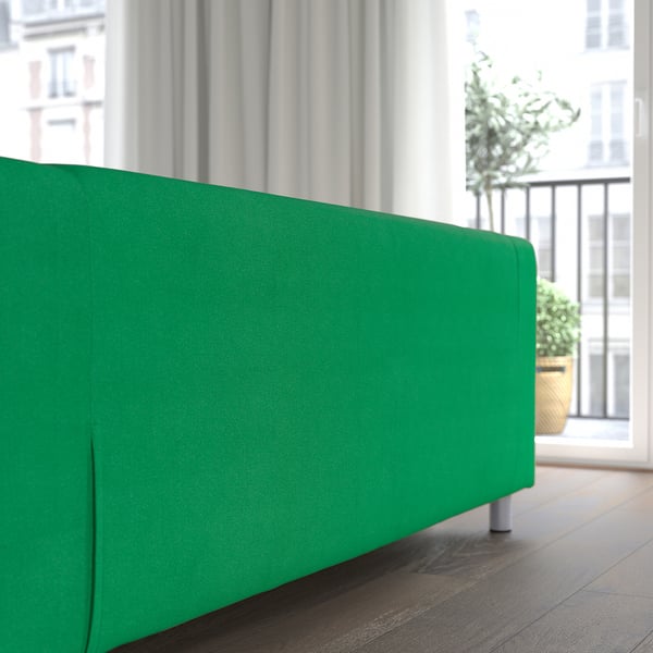Bright green couch near large window with white curtains.