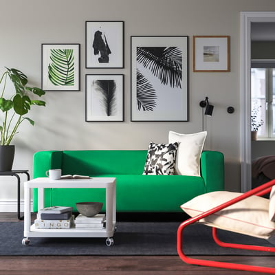 Living room with green sofa, black-and-white art, white coffee table, red chair, dark rug.