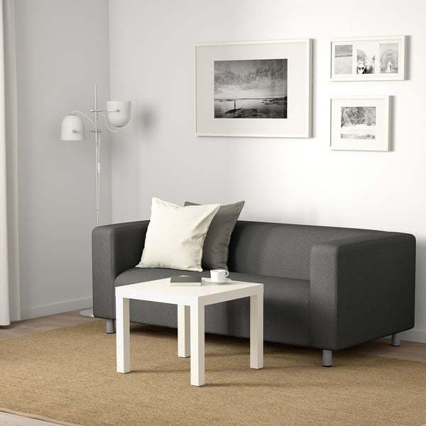 Modern living space with grey KLIPPAN sofa, white coffee table, and floor lamp. Three framed photos decorate the white wall behind.