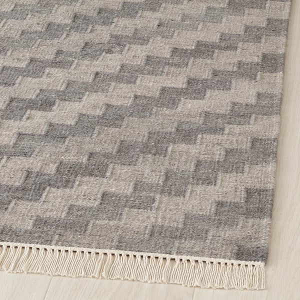 Soft, handwoven rug with grey and white patterns, cream fringe. High-quality wool and cotton blend.