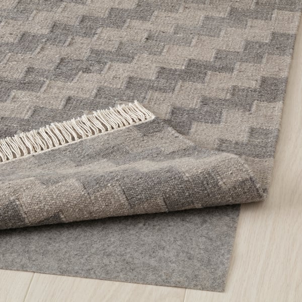 Grey wool rug with fringe, folded on light wooden floor