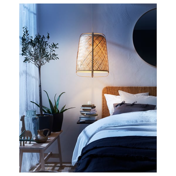 Cosy bedroom with KNIXHULT lamp, wicker bed, and bedside table with books & plants.