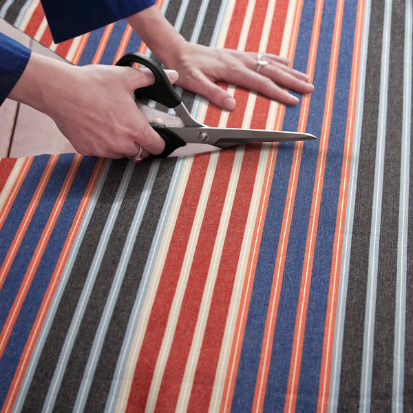 A person cuts colourful striped fabric with scissors, preparing it for sewing projects like curtains or decorations.