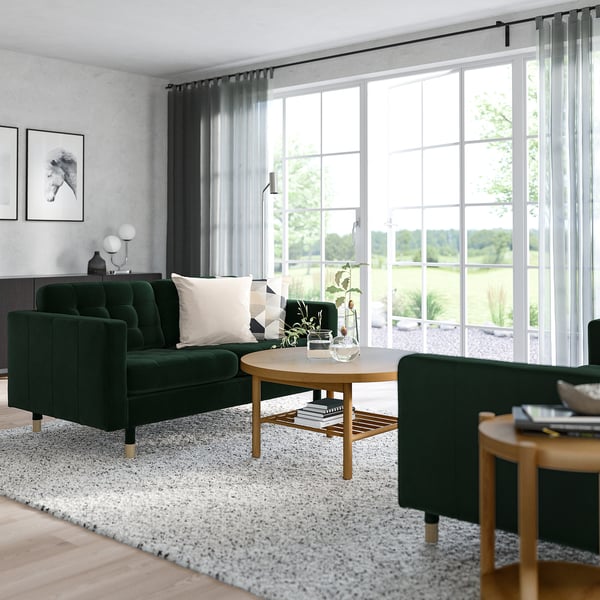 Modern living room with green velvet landskröna sofa, white rug, wooden table, and large windows. Sofa is medium-sized compared to room.