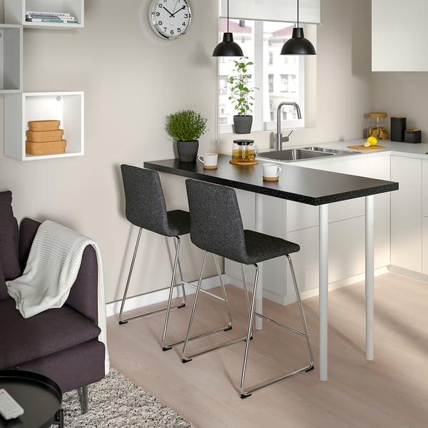Modern kitchen with two grey bar stools at sleek counter, plants, cups, cosy chair.