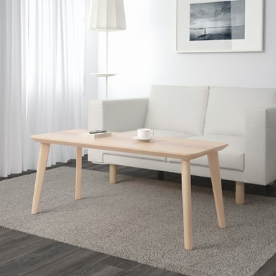 Minimalist living room with wooden coffee table, mug, notepad. Grey sofa, lamp, striped rug.