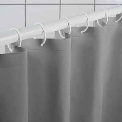 A grey shower curtain hangs from white rings, demonstrating how it effectively repels water to keep the bathroom dry.
