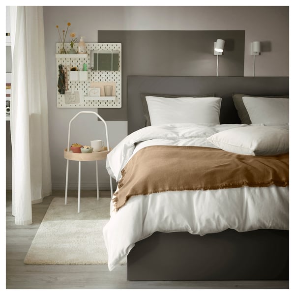 Modern bedroom with MALM bed, featuring a grey headboard, white linens, wooden tray on a side table, and a pegboard with decorative items.