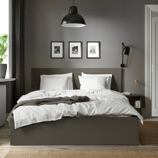 Modern bedroom with grey MALM bed, white linens, dark side tables, lamps, plants, and black-and-white photos.