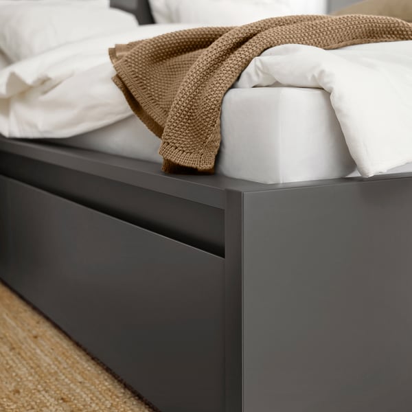 A sleek, modern bed with a beige blanket, a white pillow, and a tissue box on it, showcasing the high-quality design of the MALM bed frame.