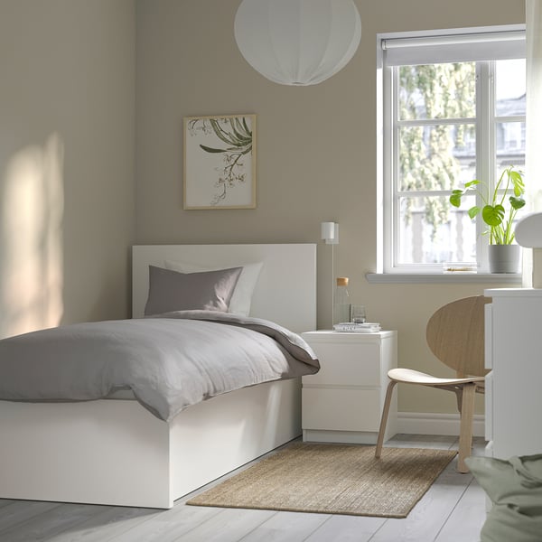 Minimalist bedroom with white MALM bed, grey linens, beige rug, floral art, and white light.